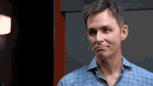 a man in a blue plaid shirt is making a face with the letters dd below him