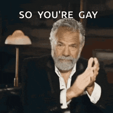 a man with a beard is clapping his hands with the words so you 're gay behind him