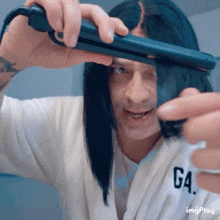a man with long black hair is holding a hair straightener in his hand