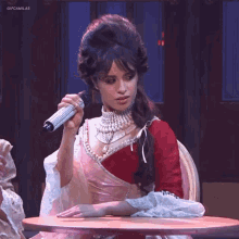 a woman in a red and pink dress is holding a microphone while sitting at a table .