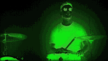a man in a white shirt is playing drums in a green light