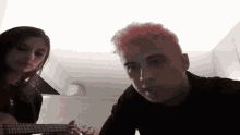 a man with pink hair playing a guitar next to a girl