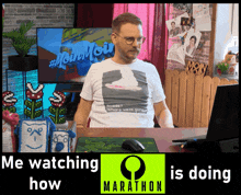 a man wearing a t-shirt that says #moinmoin stands in front of a computer