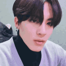 a close up of a person 's face wearing a purple sweater and black turtleneck .