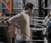 a man in a tan sweater stands with his hands on his back