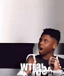 a young man is sitting on a couch with his mouth open and the words wtf written on the screen .