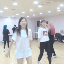 a group of girls are dancing together in a room . one girl is wearing a white shirt with a picture of a dog on it