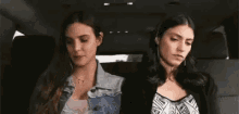 two women are sitting in the back seat of a car looking at each other .