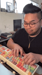 a man wearing glasses and a black shirt is typing on a colorful keyboard