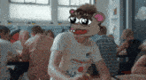 a man wearing a cartoon mouse mask is sitting at a table with other people