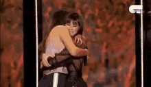 two women hugging each other on a stage in front of a microphone .
