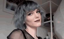 a woman with blue hair and red lips is standing in front of a white shelf
