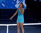 a woman in a blue tank top and shorts is singing into a microphone on a tennis court