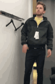 a man is standing in a dressing room wearing a green jacket and black jeans