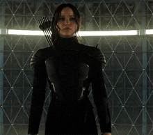a woman holding a bow and arrow stands in front of a wall