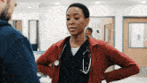 a woman wearing a red jacket and a stethoscope around her neck is talking to a man in a hospital .