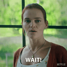 a woman with a necklace and a cardigan says wait