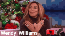 wendy williams is sitting in front of a christmas tree with her hands folded