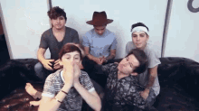 a group of young men sitting on a couch with one wearing a fedora