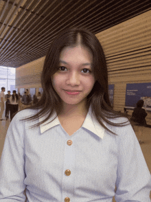 a woman in a blue striped shirt with gold buttons smiles for the camera