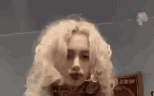a woman with blonde curly hair and red lips is smoking a cigarette in a room .