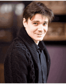 a man wearing a black sweater and black shirt smiles for the camera