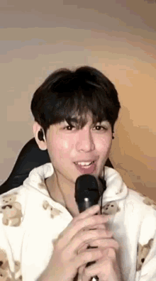 a young man is singing into a microphone while wearing a teddy bear hoodie .