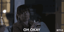 a woman sitting on a couch holding a glass of wine with the words oh okay below her