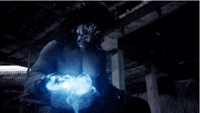 a man is standing in a dark room with blue smoke coming out of his hands