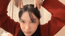 a woman in a red sweater is making a funny face with her hands in her hair .