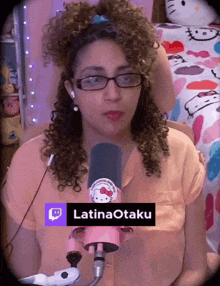 a woman with curly hair is wearing glasses and a hello kitty shirt and has a twitch logo on her shirt