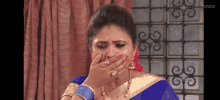 a woman in a blue saree is covering her mouth with her hand .