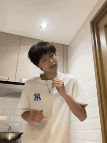 a young man wearing a white ny t-shirt is dancing in a kitchen