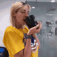 a woman in a yellow shirt is drinking from a cup