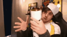 a man wearing a hat and a white shirt is holding a roll of paper towels in his hands .
