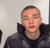 a young man with a shaved head is wearing a black jacket .