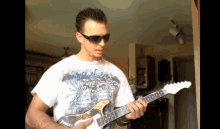 a man wearing sunglasses is playing a guitar with a shirt that says ' sniper ' on it