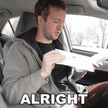 a man in a car is holding a piece of paper and the word alright is on the bottom