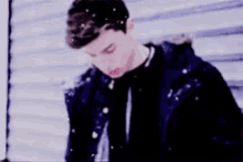 a young man in a blue jacket is standing in the snow looking down .