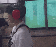 a woman wearing ear protectors stands in front of a window