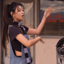 a woman in overalls stands in front of a store that says electronics