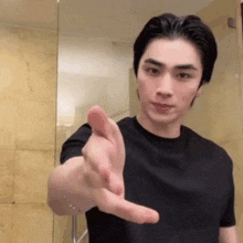 a young man in a black t-shirt is making a hand gesture .