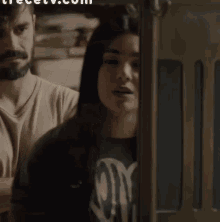 a man with a beard stands next to a woman in a dark room with the website trecetv.com in the background