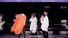 a group of men are standing on a stage and one of them is wearing a red cape .