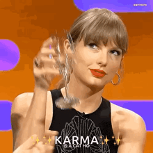 a woman in a black tank top is holding a glass with the words karma is a cat ho written on it .