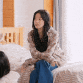 a girl in a plaid shirt sits on a bed with her legs crossed