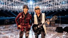 two men standing next to each other one holding a guitar