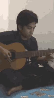 a young man is playing an acoustic guitar while sitting on a bed