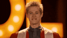 a young man wearing a red and white robe smiles in front of a yellow sign