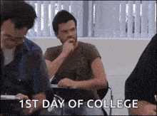 a man is sitting at a desk in a classroom with the words `` 1st day of college '' above him .